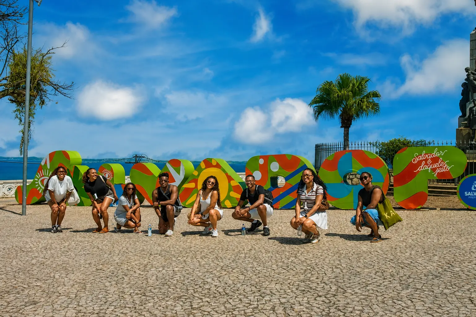 Group of friends crouching in front of the colourful Salvador letter sign by the sea