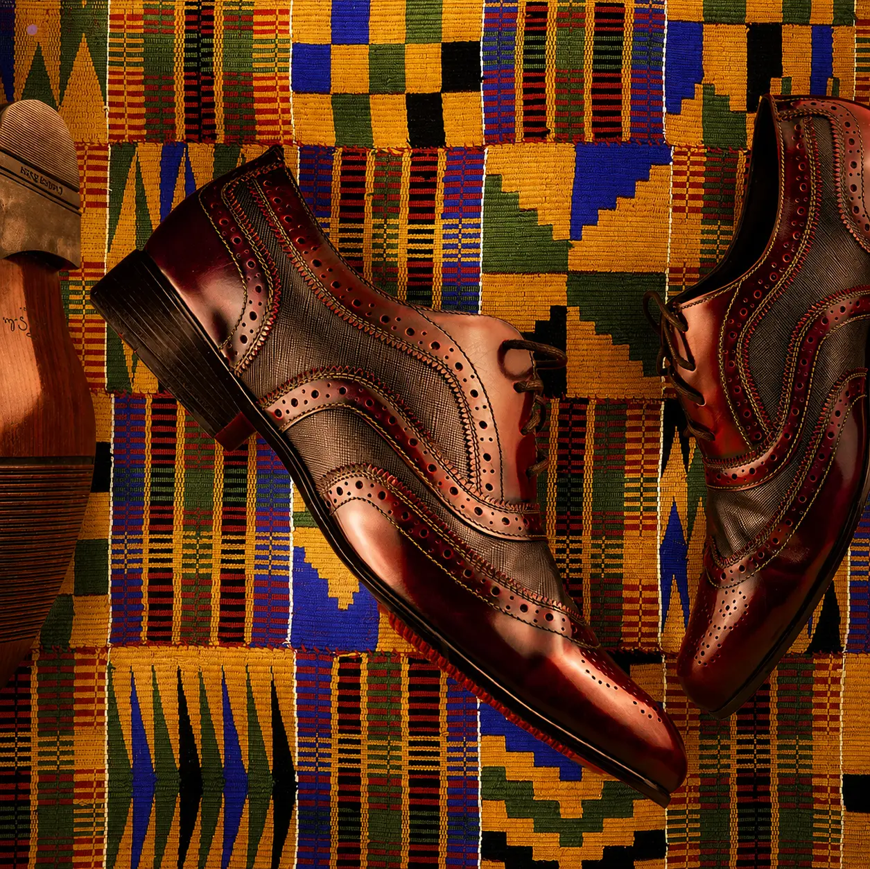 Pair of oxblood leather brogues shot flat lay on a woven kente cloth with a wooden shoe tree