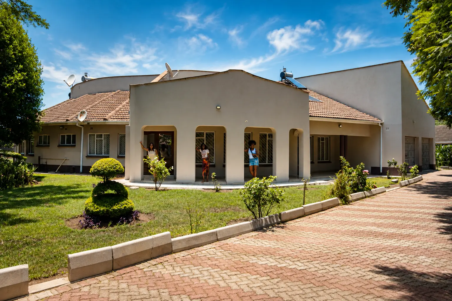 Three friends waving from the arched veranda of a sunlit family home in Zimbabwe