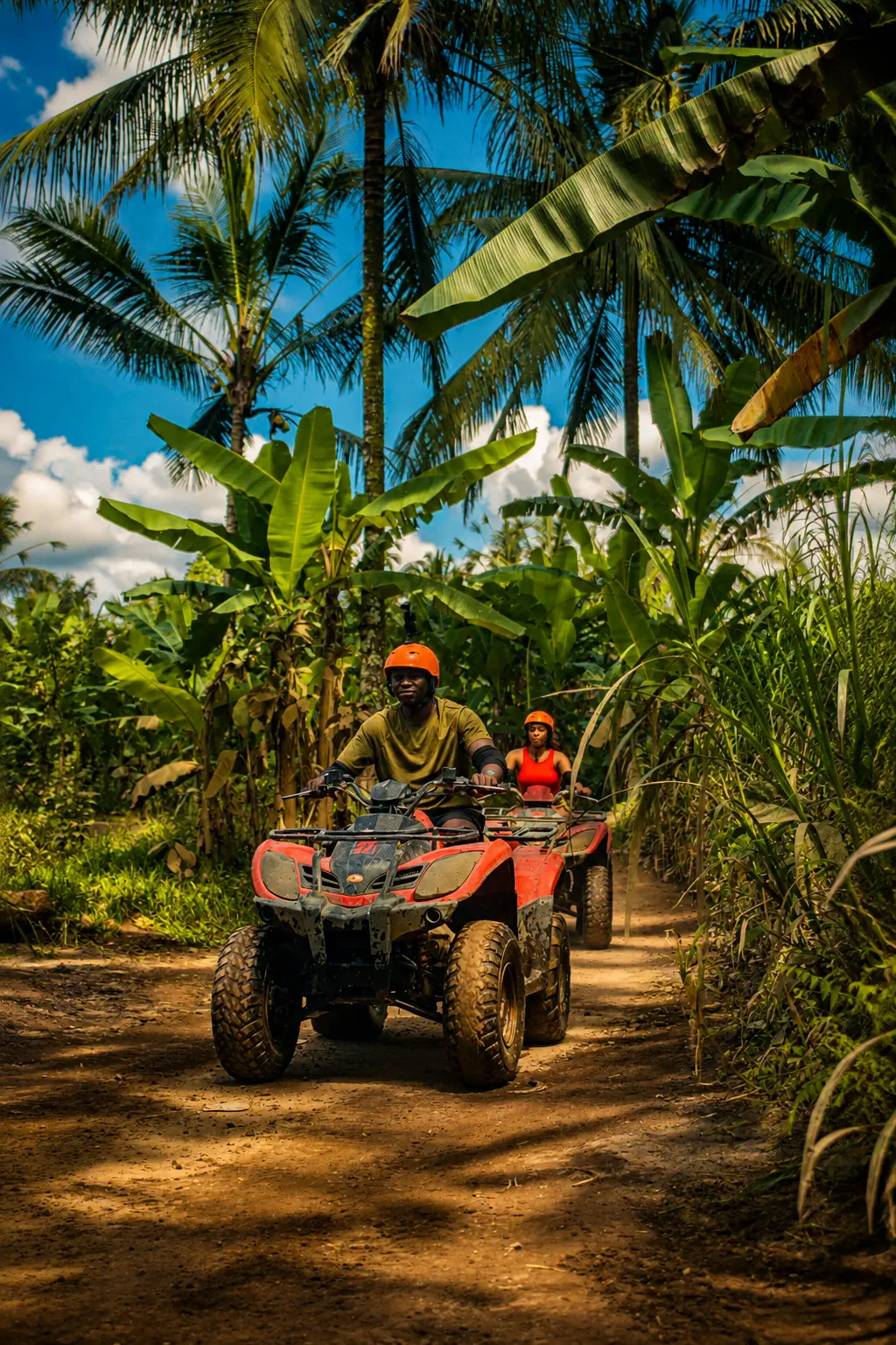 Two riders on quad bikes on a jungle track lined with palms and banana leaves in Bali