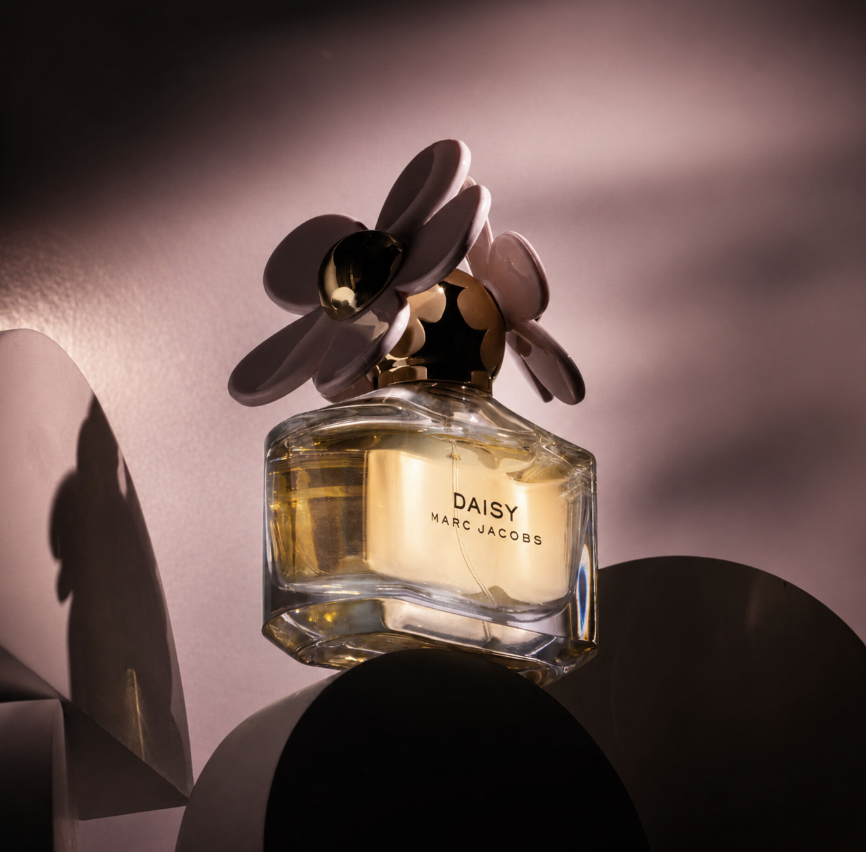 Marc Jacobs Daisy perfume bottle lit with soft pink light and paper petal shadows