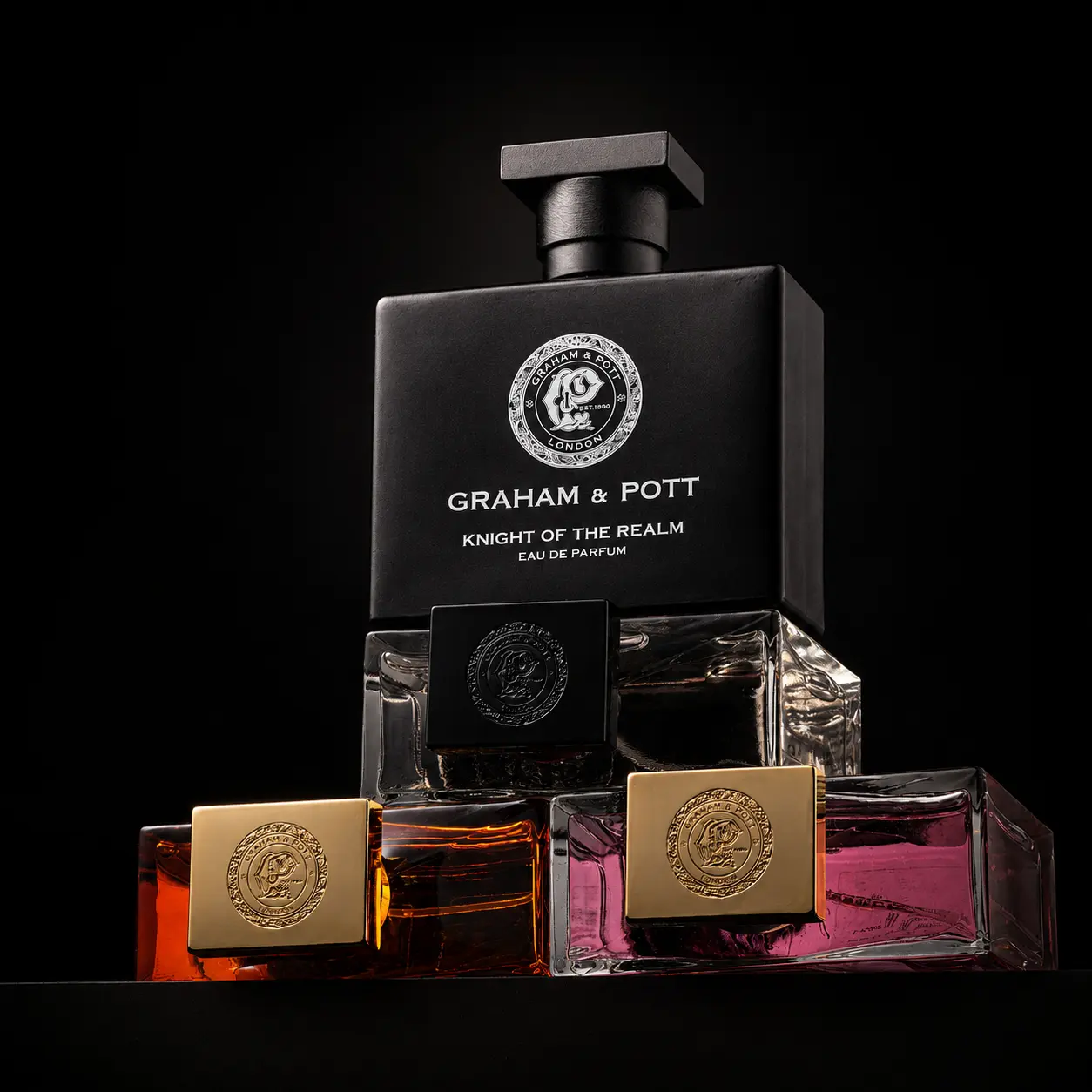 Stacked Graham and Pott fragrance bottles with gold caps lit against pure black