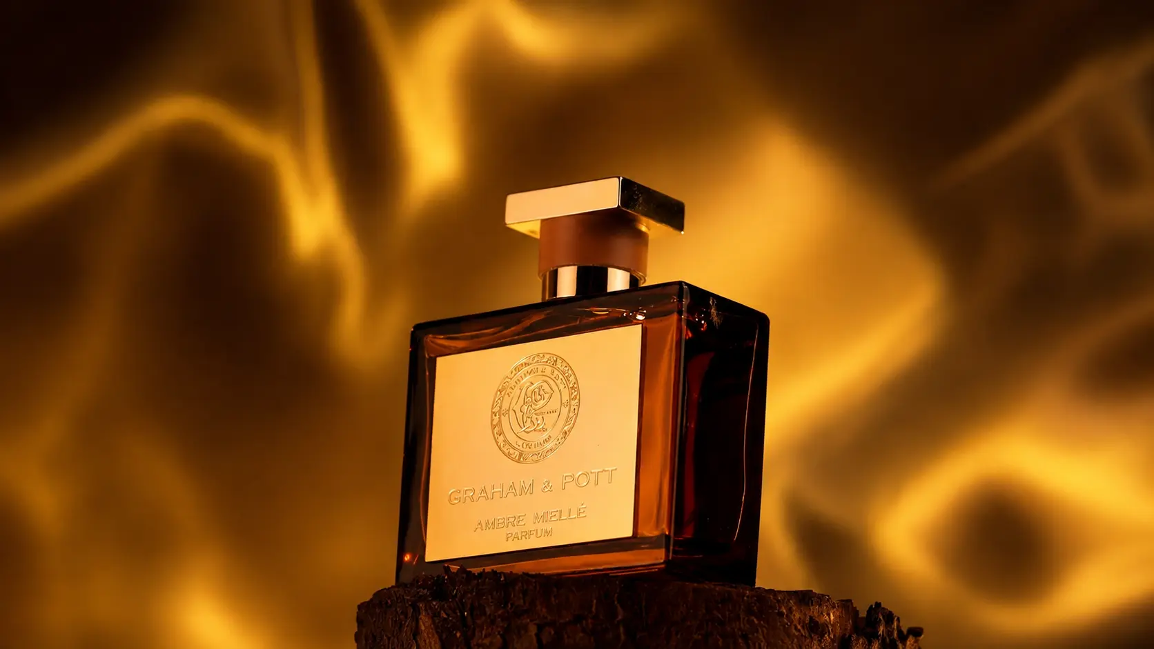 Amber perfume bottle on a wooden plinth against a swirling gold light backdrop