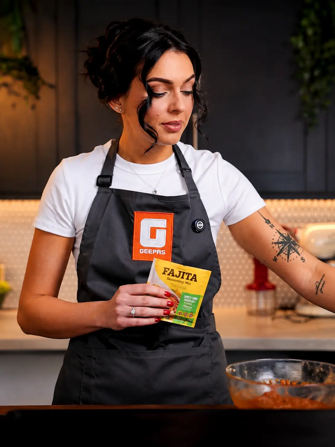 Presenter in a Geepas apron holding a fajita seasoning sachet toward the lens